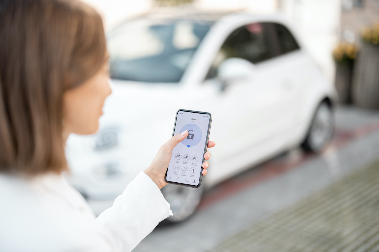 Mobile Access Control. Woman closes the door or turns on the car alarm with a mobile phone. Device with running program for vehicle security. Innovative technologies in car security and access