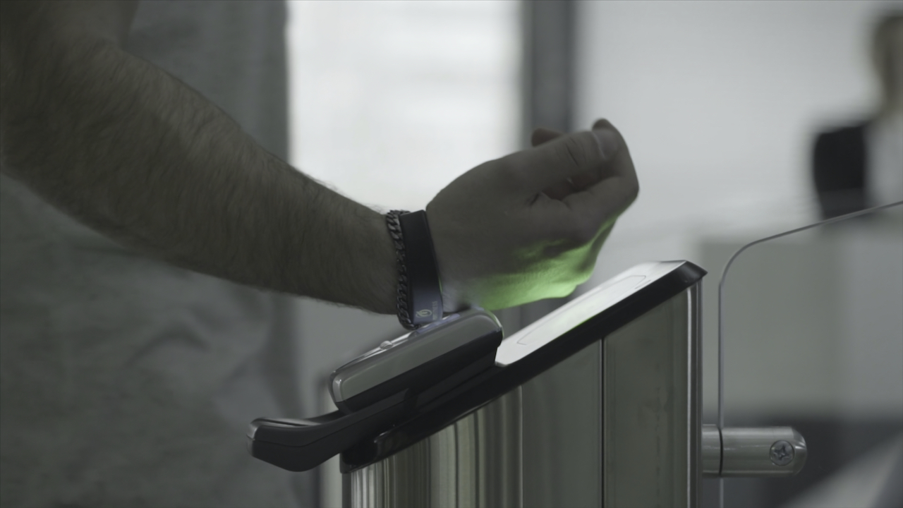 Man applying RFID bracelet to the electronic access equipment on entrance gate to the subway, underground or gym. Frame. Black electronic bracelet for access to the subway, underground or fitness center applied to the turnstile.