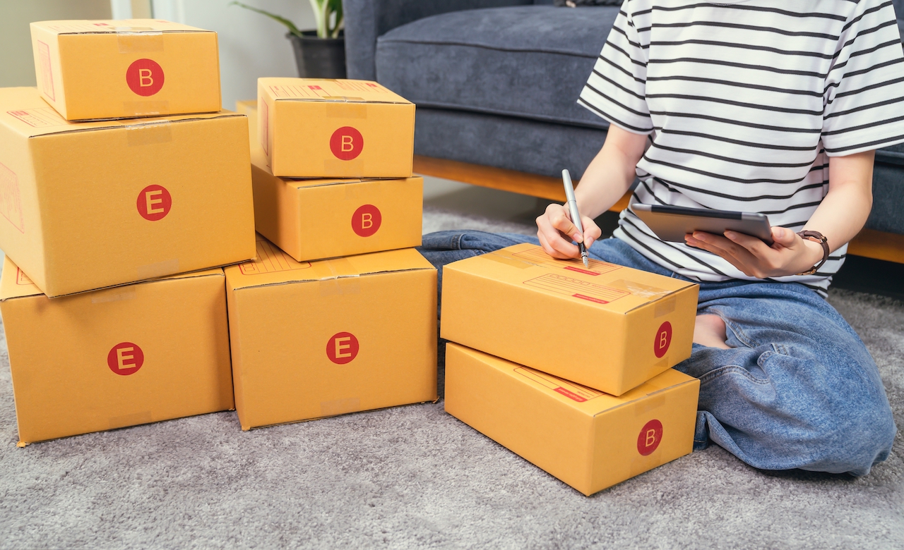 Startup small business concept, young woman owner working and packing on the box to customer at the sofa in home office, seller prepares the delivery.