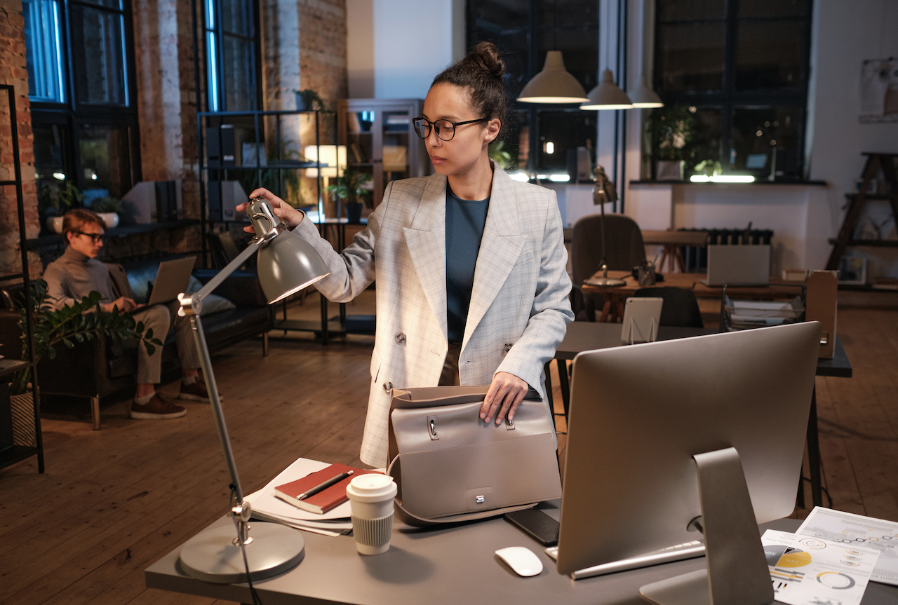 A woman in an office turning off a lamp to leave the office to be sustainable and set an example to be eco-friendly in a workplace management system.