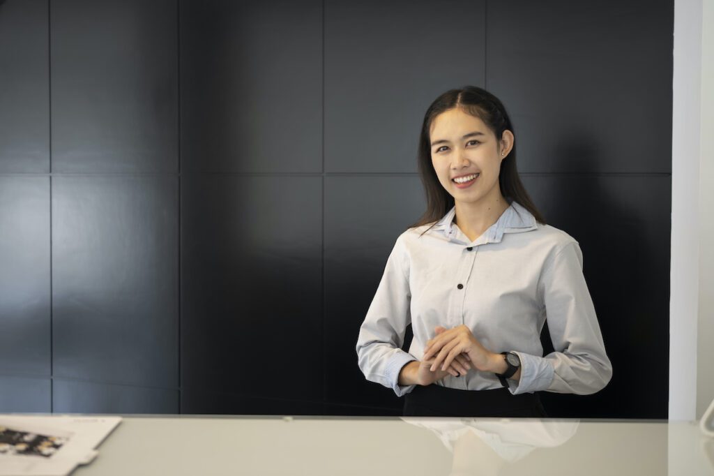 Young asian woman receptionist standing at reception desk and smiling to welcome visitors to the hotel.