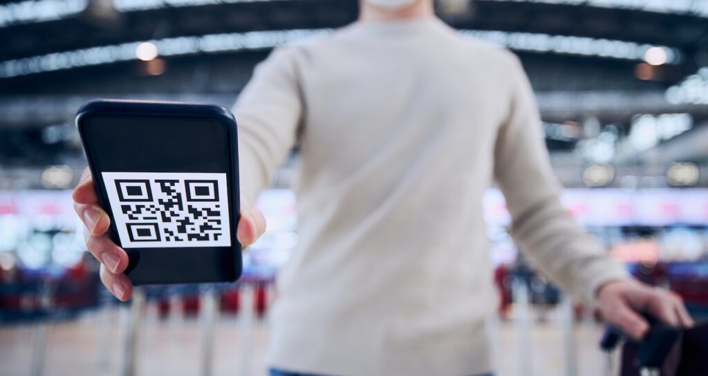 Man wearing face mask and holding smart phone with QR code at a turnstile for pre-registration for visitor management.