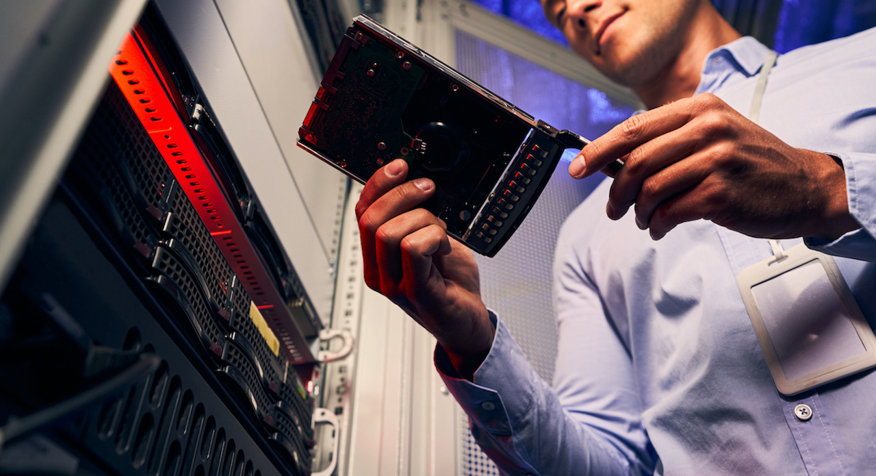 Low angle of serious system administrator staring at hard disk drive in his hands for preventive maintenance.