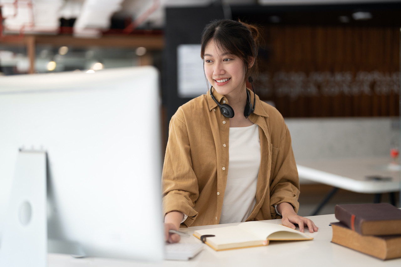 Hipster asian girl school student with wear headphone write notes watch video online webinar learn on laptop