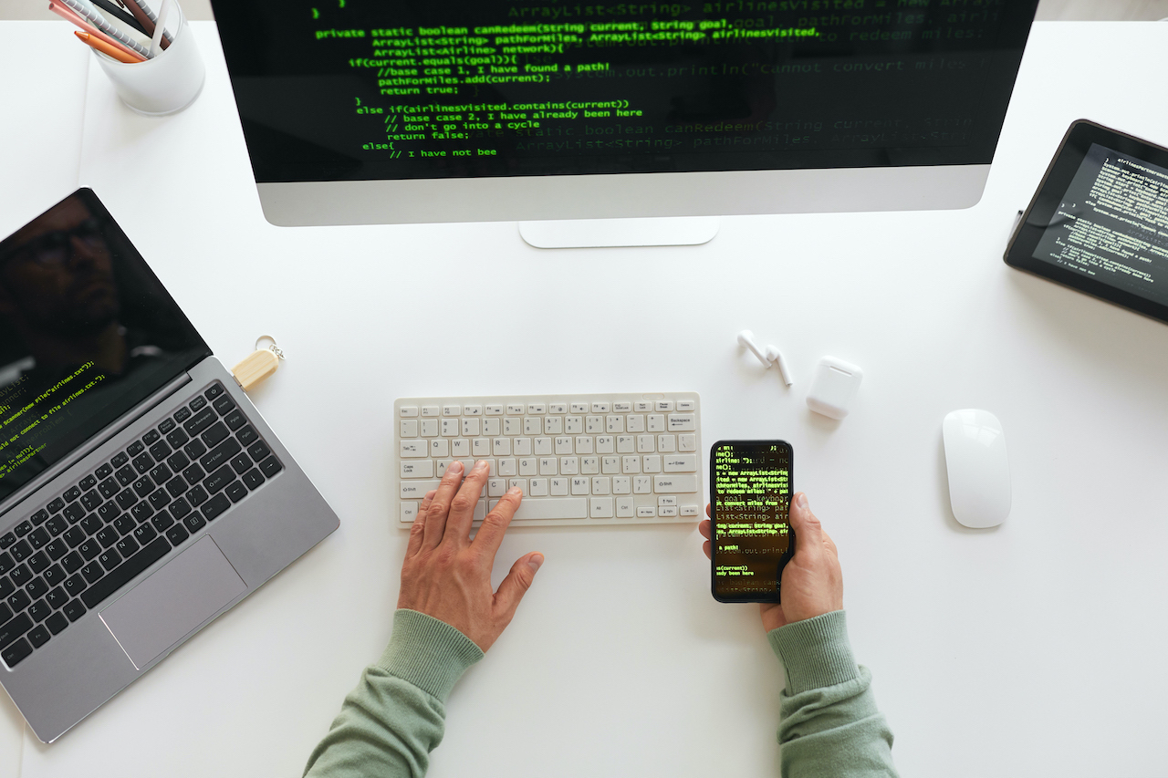 High angle view of programmer sitting at the table using computer laptop and mobile phone programming website design