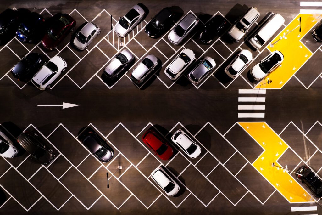 Parking Management System - Drone aerial view of parking lots with cars at night. Crowded shopping mall outdoor car park.