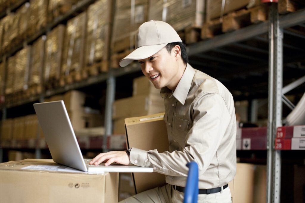 Warehouse Management System. Male Chinese warehouse worker using a laptop