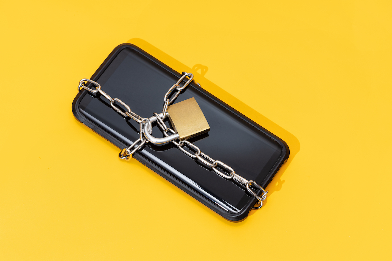 Phone security concept. Smartphone locked with chain and padlock on yellow background. Mobile security and data privacy
